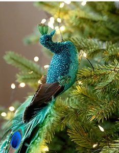 Detail of glittered teal peacock ornament with real feathers on a Christmas tree branch