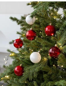 Detail of red and white 6cm Christmas ball ornaments with gold caps on a lit green tree