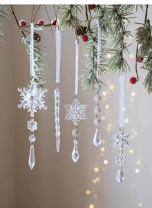 Close-up of 5-piece clear Christmas icicle and snowflake ornaments on pine branches
