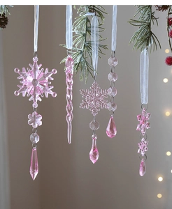 Pink acrylic Christmas icicle and snowflake ornaments hanging on festive pine branches