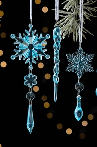 Macro shot of transparent blue snowflake and icicle ornaments hanging on a pine branch