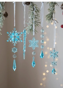 Detail of five ice blue acrylic snowflake and icicle ornaments hanging on a pine branch