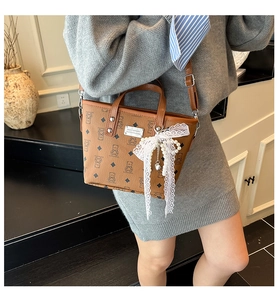 Détail d'un sac cabas marron à motif d'ours avec nœud en dentelle et pendentif perle