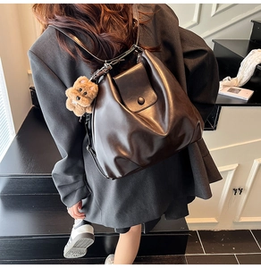 Rear view of model wearing a dark brown leather backpack with a plush bear charm