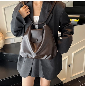 Detail of dark brown leather shoulder bag with flap closure on a model in gray blazer