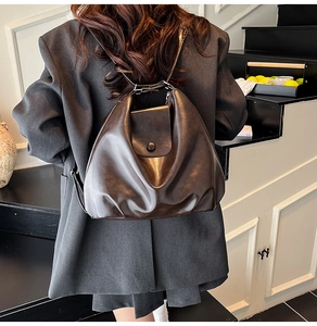 Rear view of a model wearing a large dark brown leather cloud backpack with flap closure