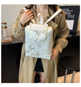 Detail of white mini backpack with lace edges, bow charms and butterfly prints