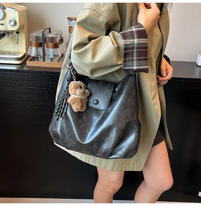 Close-up of retro grey leather shoulder bag with bear charm in casual cafe setting