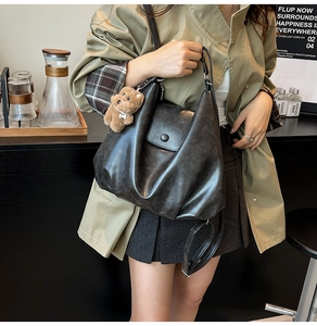 Detail of black matte PU hobo bag with soft pleated texture and brown plush bear charm