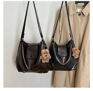 Detail view of matte leather shoulder bags featuring a buckle closure and plush puppy pendant