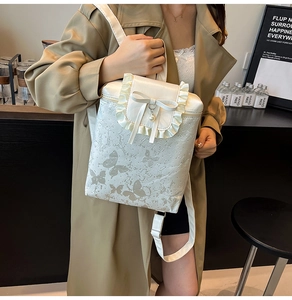 Detail of white butterfly backpack with ruffled edges, lace bow, and pearl pendant
