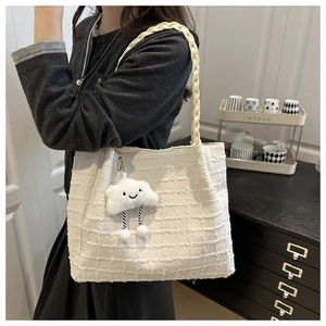 Close-up of white tweed tote bag featuring braided handles and a plush cloud charm detail