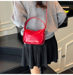 Detail view of glossy red leather crossbody bag with fashion embossed label and gold chain