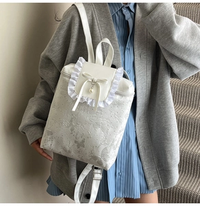 Detailed view of white pleated lace backpack with butterfly embossing and pearl bow charm
