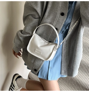 Sac bandoulière blanc minimaliste avec chaîne porté par un mannequin en extérieur