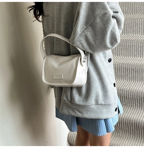 Close-up of a white leather crossbody bag with chain strap and Fashion metal plaque