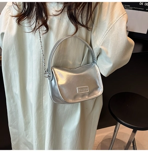 Close-up of a silver metallic crossbody bag with a round handle and fashion metal plate