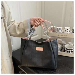 Detail of black quilted tote bag with pink handles and silver chain link accents