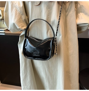 Detail of black glossy cylindrical crossbody bag with chain strap and Fashion label