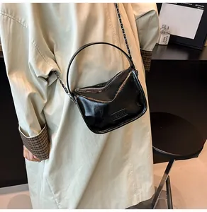 Détail de la surface en cuir verni noir brillant et de la bandoulière en chaîne du petit sac