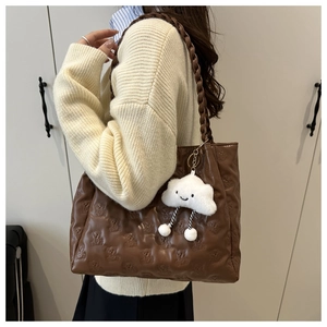 Brown tote bag detail with bear embossed pattern, woven strap, and cloud charm accessory