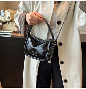 Detail of a black patent leather handbag with a metal chain strap and logo plaque