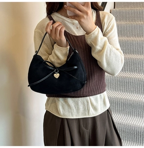 Close-up of black suede hobo bag with leather bow and golden heart pendant detail