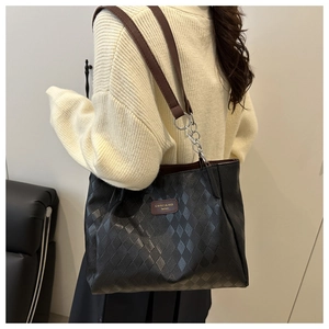 Close-up of quilted black tote bag with brown strap and silver chain hardware details