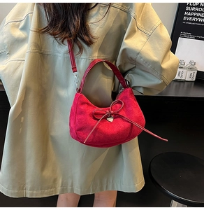 Dettaglio della borsa rossa in camoscio con fiocco e cuore abbinata a un trench coat