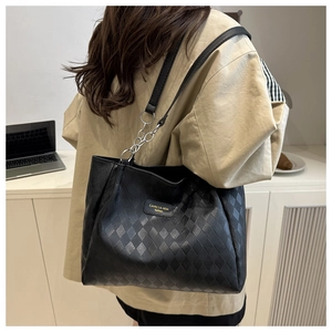 Detail of black tote bag with quilted leather texture and silver chain strap on a model