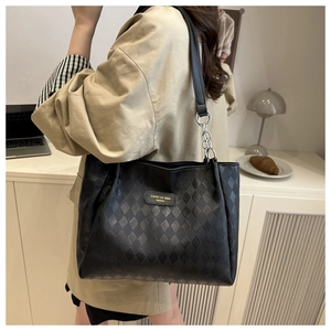 Detailed view of black quilted tote bag with gold logo and leather chain strap shown on model