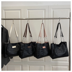 Close-up of quilted tote bags with colorful straps and metal chain detail on white wall