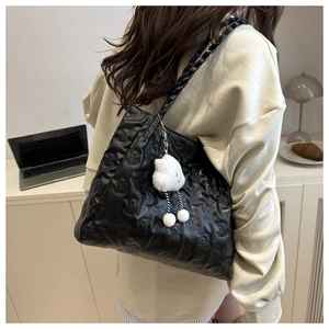 Close-up of black tote bag featuring embossed bear patterns and a white cloud plush charm
