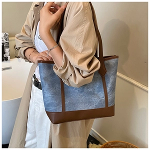 Blue denim texture tote bag with brown leather trim shown on a model in a trench coat