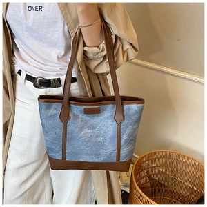 Detail of blue washed texture tote bag with brown leather trim and fashion patch