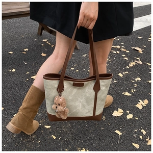 Detail of canvas tote bag with brown leather trim and a cute plush dog pendant charm