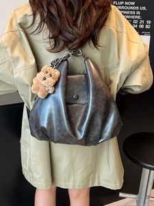Dark grey soft leather hobo bag with plush bear charm worn by a model in a lifestyle setting