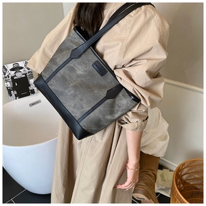 Detail of grey canvas tote bag with black leather trim worn with a beige dress