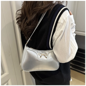 Detail of silver metallic underarm bag with a gold bow buckle on a crescent shoulder strap