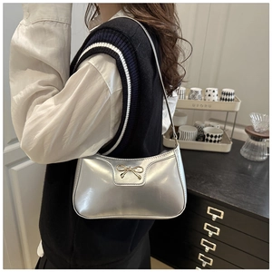 Detail of silver metallic shoulder bag with gold bow clasp and sleek leather strap