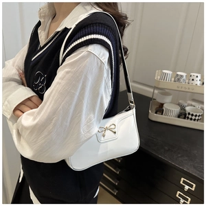 White patent leather shoulder bag with golden bow clasp worn by a model in a modern room