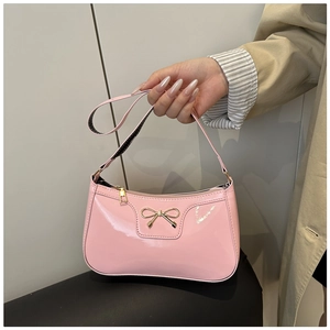 Close-up of pink patent leather handbag with gold metal bow held by model in trench coat