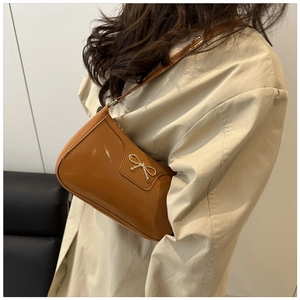 French vintage brown patent leather shoulder bag with golden bow buckle on beige coat