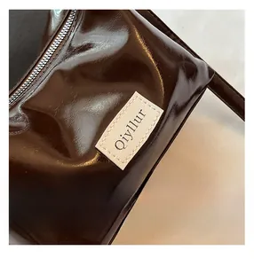 Detailed close-up of dark brown glossy shoulder bag featuring fine stitching and brand patch