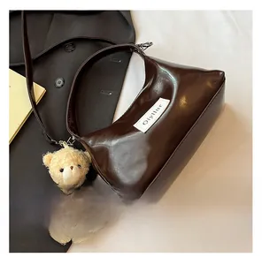 Detail of dark brown glossy underarm bag with a cute plush bear charm and brand logo