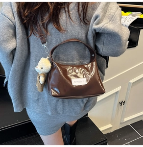 Detail of dark brown patent leather handbag with plush bear charm and brand label