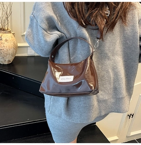 Detail of glossy brown leather shoulder bag with white brand label on the front