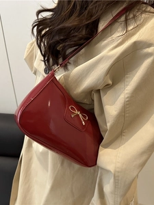Red patent leather baguette shoulder bag featuring a gold bow detail on beige trench coat