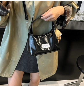 Detail of glossy black shoulder bag with brand label and cute brown plush bear charm