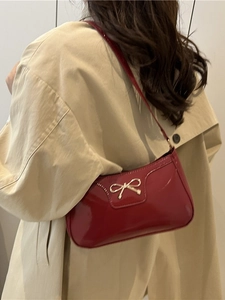 Vibrant red glossy leather underarm bag featuring a stylish gold metal bow accent